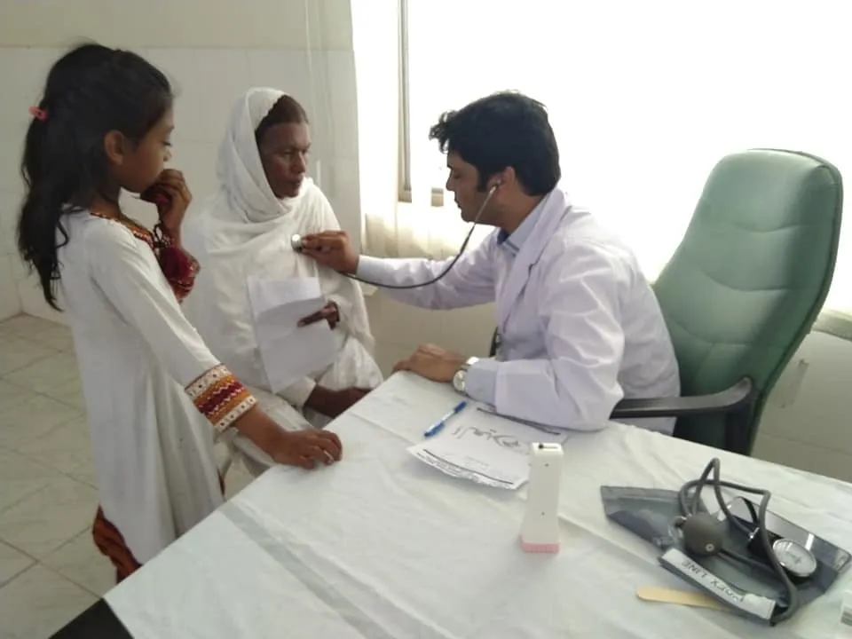 A doctor listens to a patient’s chest at the Health Mela as a young girl looks on